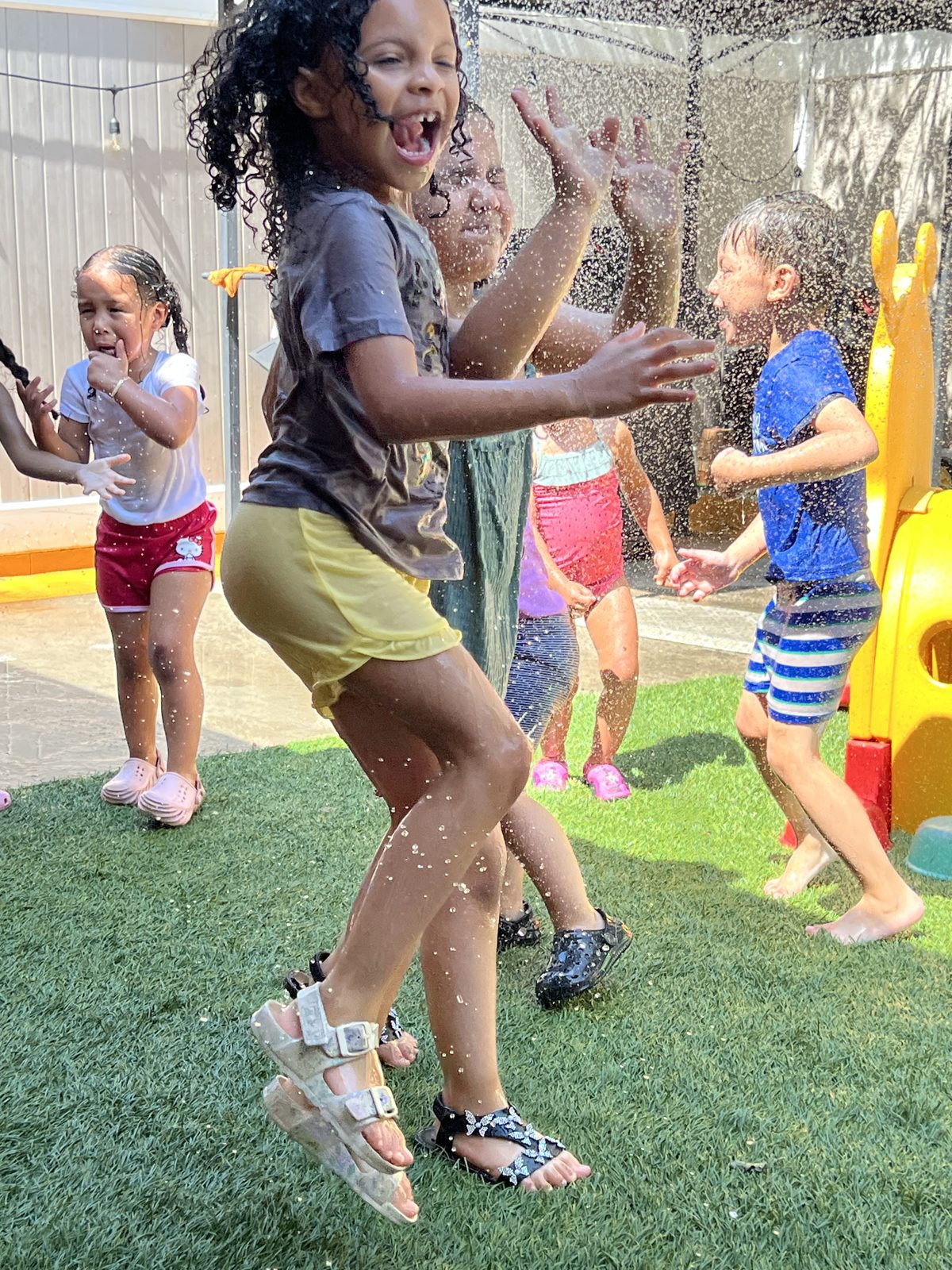Children laughing and playing in the sprinklers outdoors
